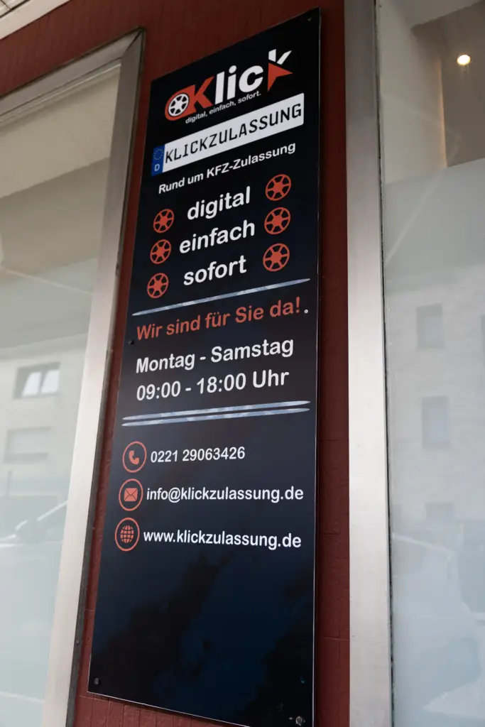 Hinweistafel im Schaufenster des Klickzulassung-Büros mit Öffnungszeiten und Kontaktdaten